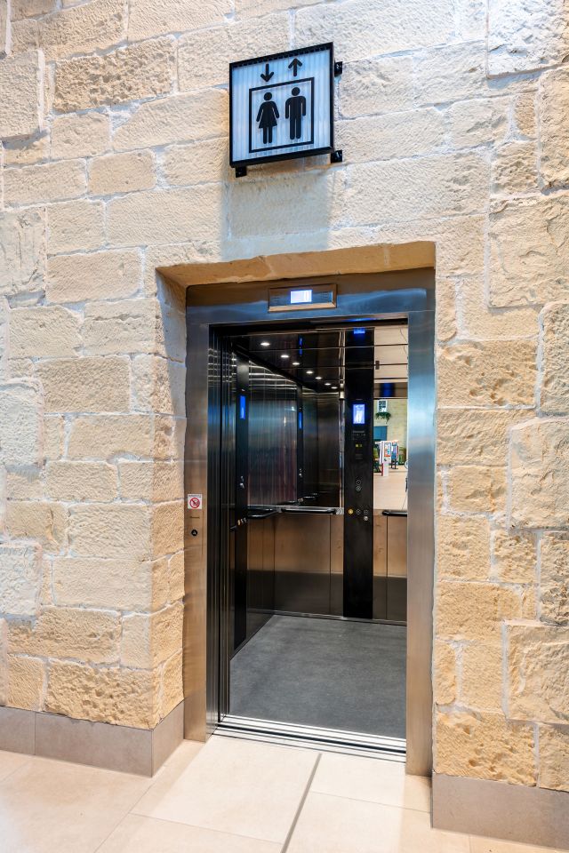 Stannah passenger lift features adjacent-opening, two-panel entrances, stainless-steel walls and premium vinyl stone black concrete floor