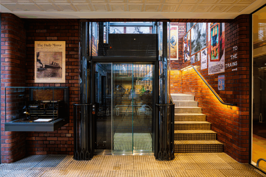 View of bespoke glass lift at ground level in train-themed cafe and cheese factory, The Creamery in Somerset